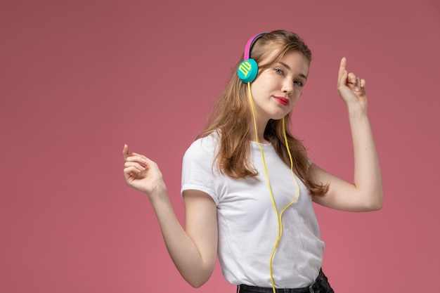 Vooraanzicht jonge aantrekkelijke vrouw in wit t-shirt dansen en luisteren naar muziek op donkerroze muur model kleur vrouwelijk jong meisje