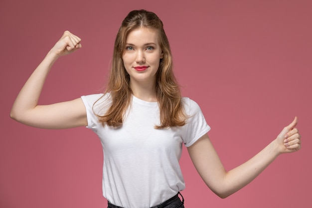 Vooraanzicht jonge aantrekkelijke vrouw in wit t-shirt en zwarte broek poseren en buigen op de roze muur model vrouw pose kleurenfoto