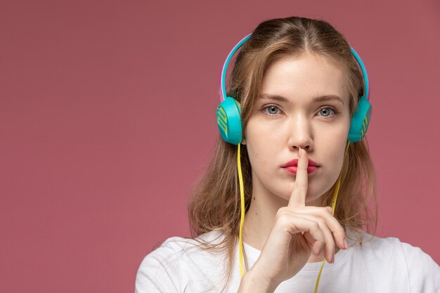 Vooraanzicht jonge aantrekkelijke vrouw in wit t-shirt luisteren naar muziek via oortelefoons op de roze muur model kleur vrouwelijke jong