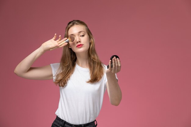 Vooraanzicht jonge aantrekkelijke vrouw in wit t-shirt make-up op roze muur doen model vrouw pose kleurenfoto vrouwelijke jong