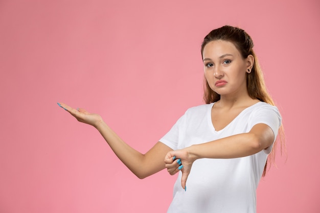 Vooraanzicht jonge aantrekkelijke vrouw in wit t-shirt poseren en tonen in tegenstelling tot teken op de roze achtergrond