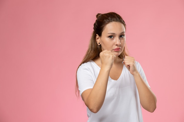 Vooraanzicht jonge aantrekkelijke vrouw in wit t-shirt poseren met bokstribune op de roze achtergrond