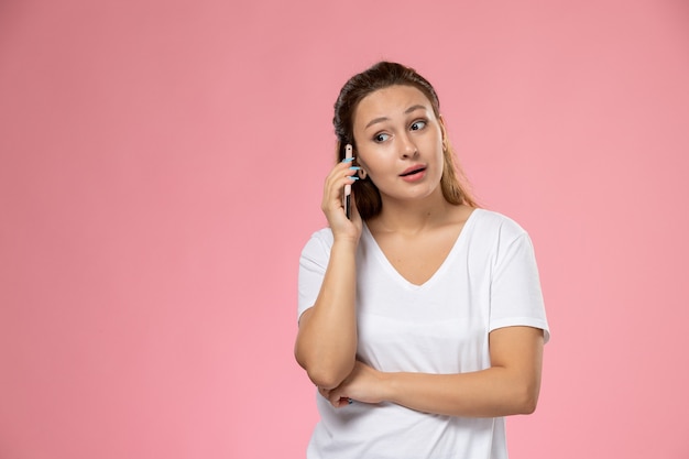 Vooraanzicht jonge aantrekkelijke vrouw in wit t-shirt praten aan de telefoon op de roze achtergrond