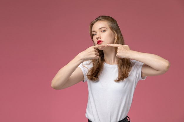 Vooraanzicht jonge aantrekkelijke vrouw in wit t-shirt wat betreft haar acne op de donkerroze muur model kleur vrouwelijk jong meisje