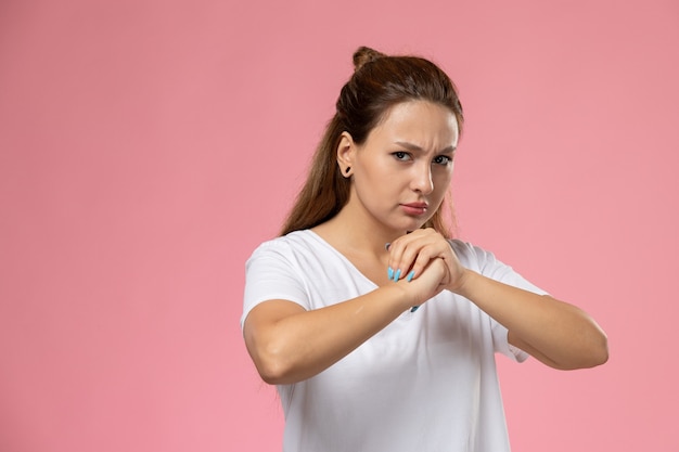 Vooraanzicht jonge aantrekkelijke vrouw in witte t-shirt boze uitdrukking op roze achtergrond