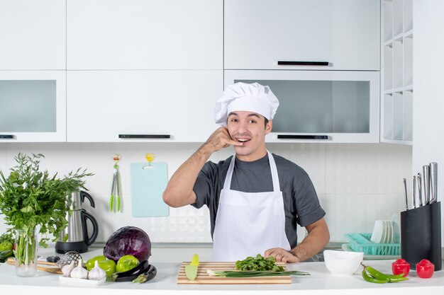 Vooraanzicht jonge chef-kok in uniform die me een telefoongebaar maakt