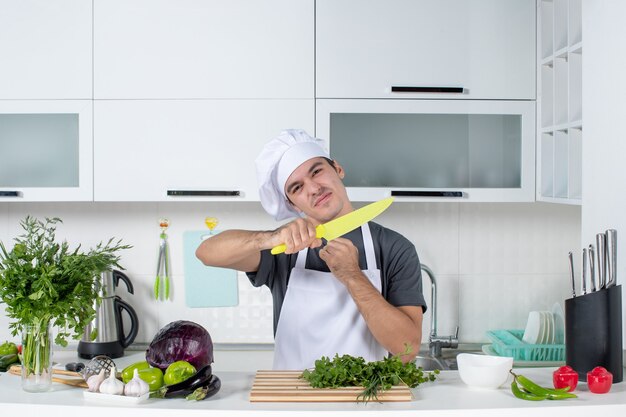 Vooraanzicht jonge chef-kok in uniform in keuken verschillende groenten op tafel