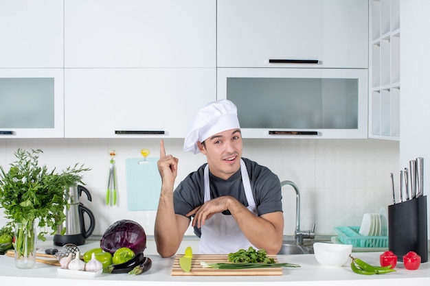 Vooraanzicht jonge chef-kok in uniforme snijgroenten op snijplank