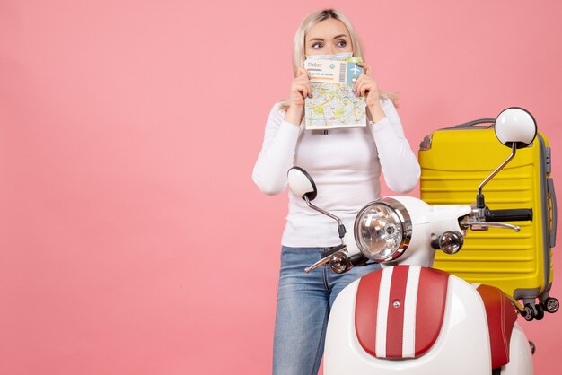 Vooraanzicht jonge dame die kaartje en kaart op haar gezicht steunt dat zich dichtbij bromfiets bevindt