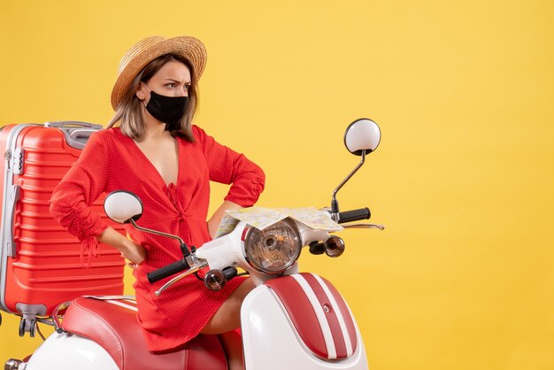 Vooraanzicht jonge dame in rode jurk op bromfiets handen op een taille zetten