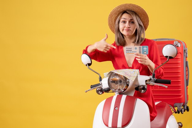 Vooraanzicht jonge dame in rode jurk wijzend op ticket op bromfiets