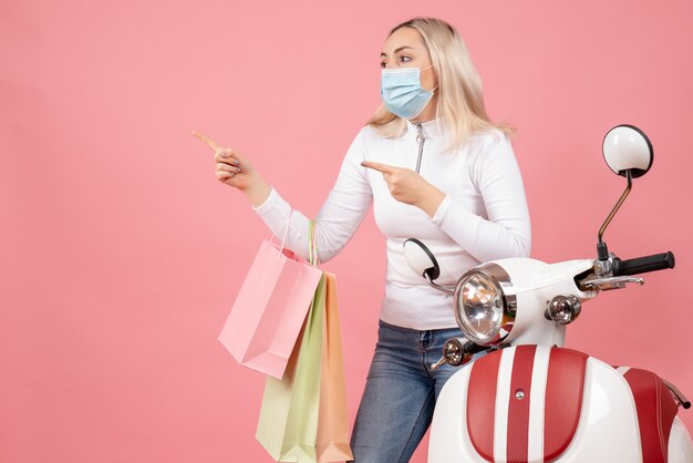 Vooraanzicht jonge dame met boodschappentassen wijzend naar links in de buurt van bromfiets