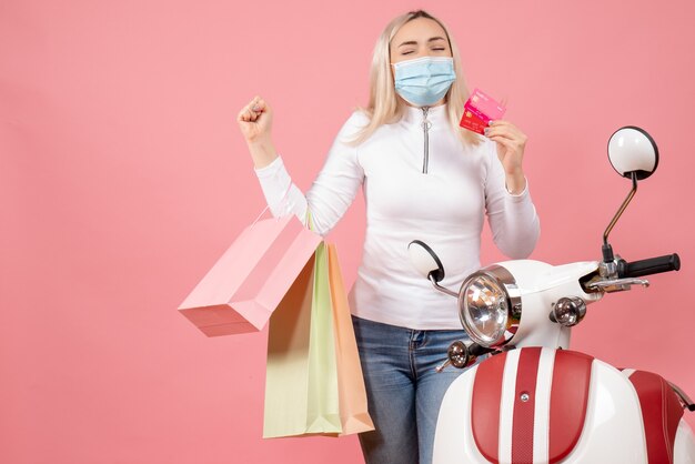 Vooraanzicht jonge dame met gesloten ogen met kaarten en boodschappentassen in de buurt van bromfiets