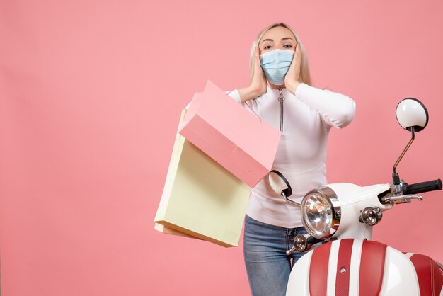 Vooraanzicht jonge dame met masker bedrijf boodschappentassen staande in de buurt van bromfiets