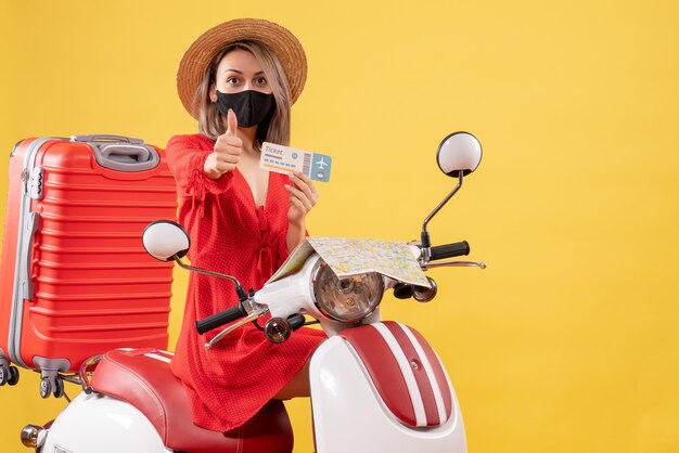 Vooraanzicht jonge dame met zwart masker op bromfiets met kaartje met duimen omhoog