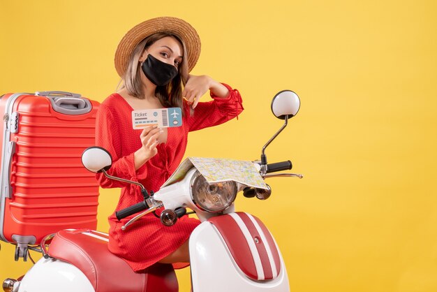 Vooraanzicht jonge dame met zwart masker op bromfiets met rode koffer met kaartje en bel me teken