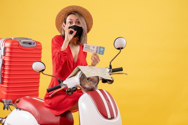 Vooraanzicht jonge dame met zwart masker op bromfiets met ticket gebarend okey teken