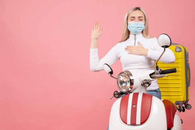 Vooraanzicht jonge dame op bromfiets met gele koffer hand op haar borst zetten en veelbelovend