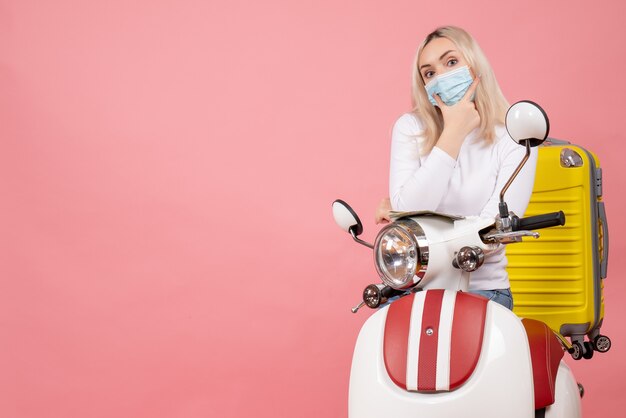 Vooraanzicht jonge dame op bromfiets met gele koffer hand op haar kin zetten