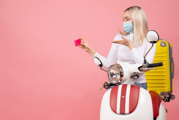 Vooraanzicht jonge dame op bromfiets met gele koffer met kaart op roze muur