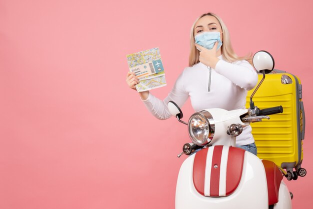 Vooraanzicht jonge dame op bromfiets met gele koffer met kaartje en kaart hand op haar kin te zetten