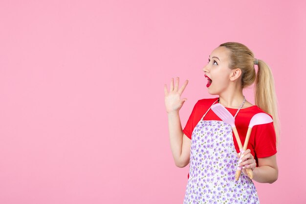 Vooraanzicht jonge huisvrouw met bestek op roze muur