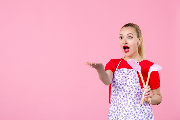 Vooraanzicht jonge huisvrouw met bestek op roze muur