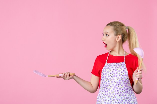 Vooraanzicht jonge huisvrouw met bestek op roze muur