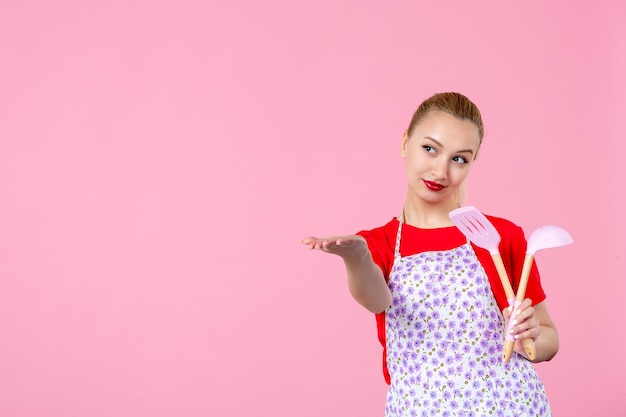 Vooraanzicht jonge huisvrouw met bestek op roze muur