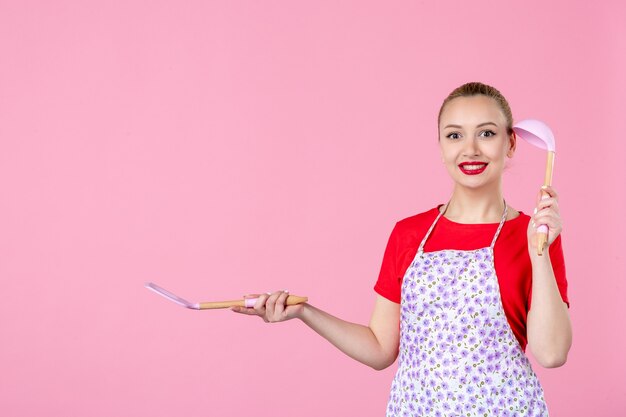 Vooraanzicht jonge huisvrouw met bestek op roze muur