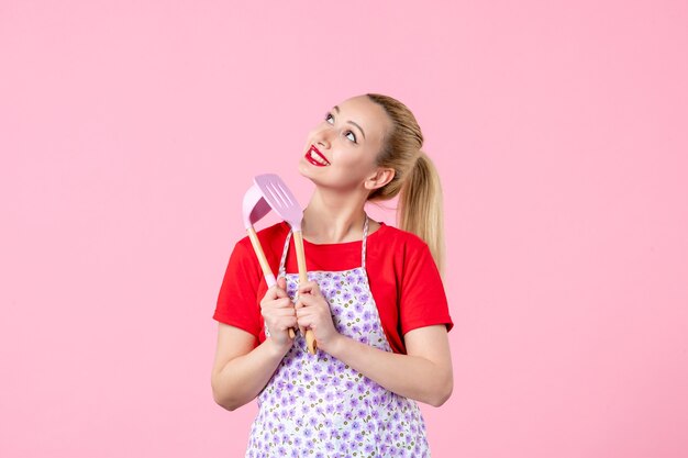 Vooraanzicht jonge huisvrouw met bestek op roze muur