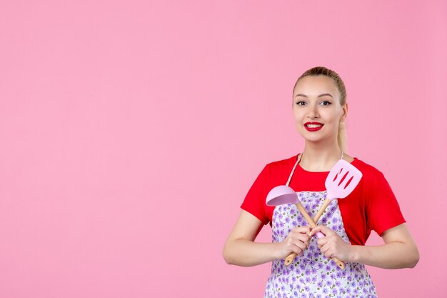 Vooraanzicht jonge huisvrouw poseren met bestek in haar handen op roze muur