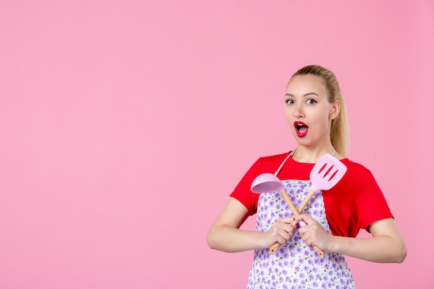 Vooraanzicht jonge huisvrouw poseren met bestek in haar handen opgewonden op roze muur