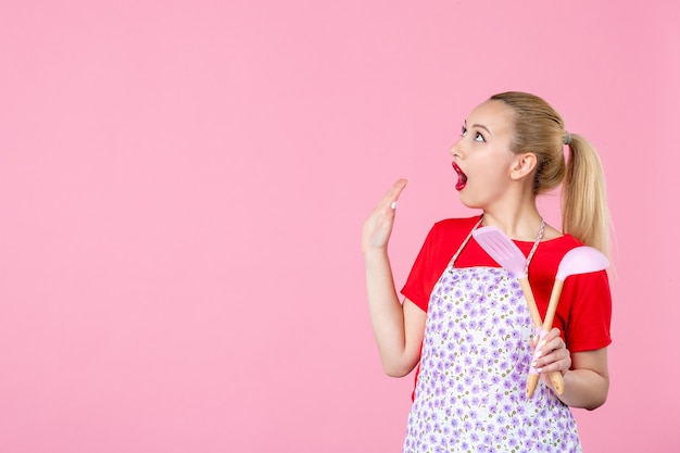 Vooraanzicht jonge huisvrouw poseren met bestek op roze muur