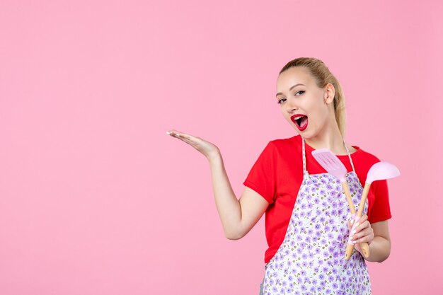 Vooraanzicht jonge huisvrouw poseren met bestek op roze muur