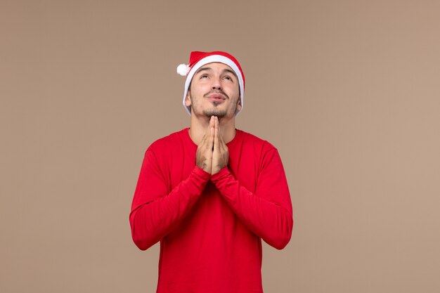 Vooraanzicht jonge man bidden op de bruine achtergrond emotie kerstvakantie