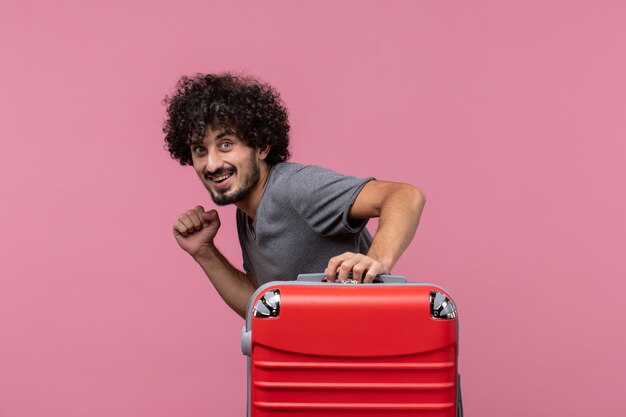 Vooraanzicht jonge man die op vakantie gaat met zijn rode tas op de roze ruimte