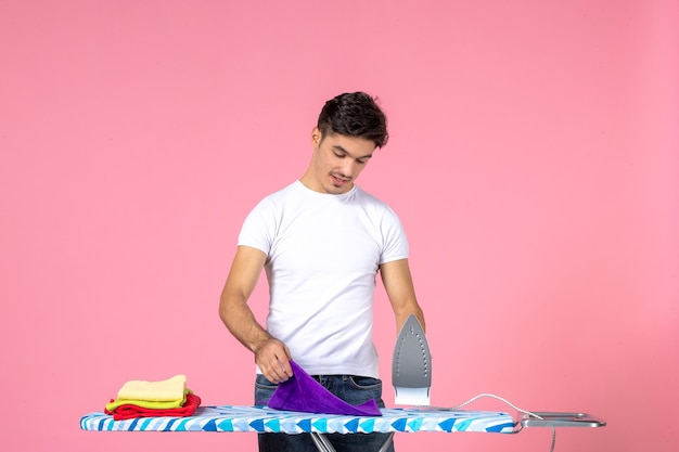 Vooraanzicht jonge man die schone handdoeken op roze achtergrond strijkt schone inspanning huishoudelijk werk man werkkleding thuis