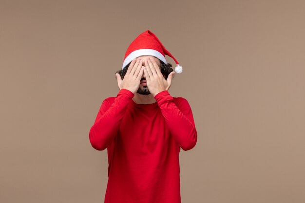Vooraanzicht jonge man die zijn gezicht op bruine achtergrond emotie kerstvakantie
