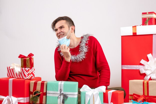 Vooraanzicht jonge man die zijn masker opstijgt rond kerstcadeaus