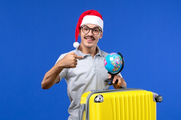 Vooraanzicht jonge man gele draagtas met globe op blauwe bureau vliegtuig vakantiereis