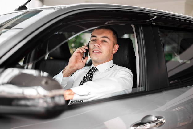 Vooraanzicht jonge man in auto praten over telefoon