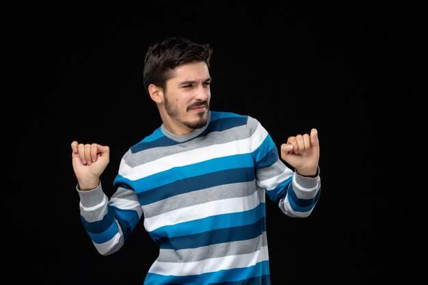 Gratis foto vooraanzicht jonge man in blauw gestreepte trui die zich verheugt op de zwarte muur