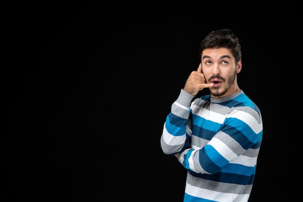 Vooraanzicht jonge man in blauw gestreepte trui op de zwarte muur