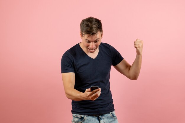 Vooraanzicht jonge man in blauw t-shirt met zijn telefoon op roze achtergrond man model emotie kleur man