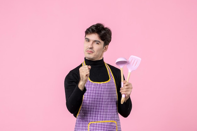 Vooraanzicht jonge man in cape met lepels op roze achtergrond beroep voedsel horizontaal uniform deeg keuken werk kleur maaltijd