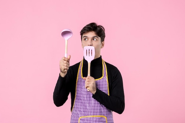 Vooraanzicht jonge man in cape met lepels op roze achtergrondkleur voedsel koken uniform horizontaal werk deeg beroep
