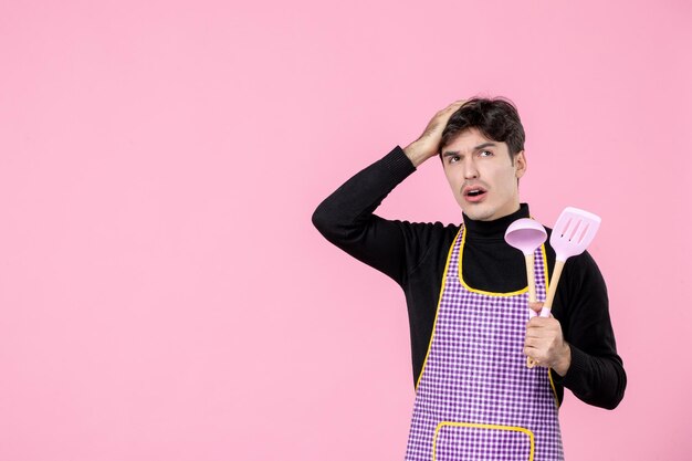 Vooraanzicht jonge man in cape met roze lepels op roze achtergrond deeg beroep keuken uniforme kleur horizontale chef koken baan werknemers