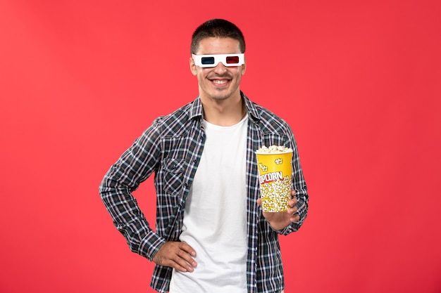 Vooraanzicht jonge man in d zonnebril met popcornpakket op het lichtrode bureau mannelijke films theater bioscoopfilm