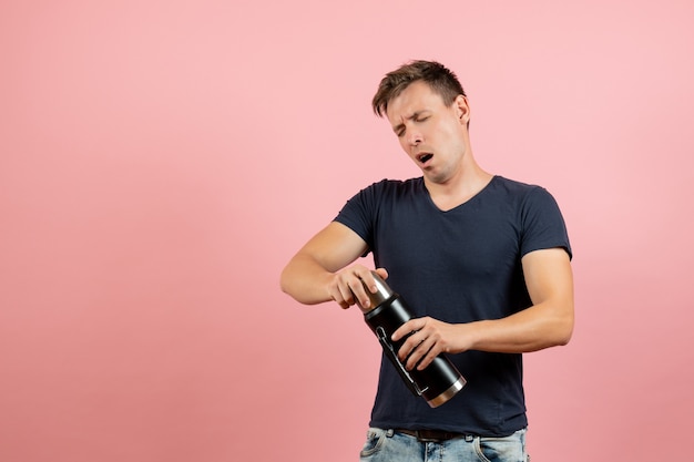 Vooraanzicht jonge man in donkerblauw shirt met thermoskan op roze achtergrond menselijke mannelijke man emotie model kleur